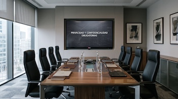 Una sala de reuniones con mesa de madera, sillas ejecutivas y una pantalla con la frase Privacidad y confidencialidad obligatorias.