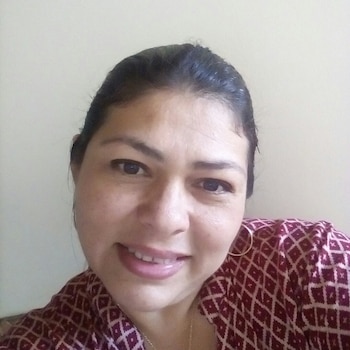 Primer plano de una mujer de cabello oscuro con pendientes de aro y blusa estampada en tono granate ante un fondo claro