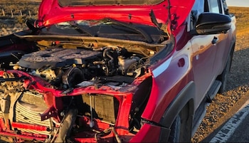 Automóvil rojo con la parte delantera destruida y el capó abierto al costado de una ruta asfaltada en una zona rural