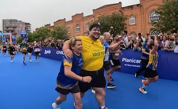 Un hombre sonriente con camiseta amarilla y una mujer sonriente con camiseta azul se abrazan mientras corren por una pista azul en un evento deportivo