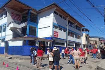 Edificio blanco y azul con letreros "CEDIF San Ramón Inabif", grupo de personas en la calle, postes con cables, casas, cielo azul y montañas en el fondo