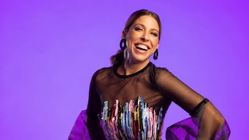 Flor Bertotti sonríe frente a un fondo morado, vestida con un atuendo negro de mangas transparentes y lentejuelas de colores en el pecho