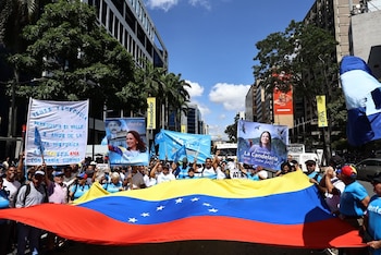 Multitud de personas portan la bandera de Venezuela y pancartas con la imagen de María Corina Machado durante una manifestación en una calle urbana