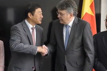 Suelo de concreto agrietado con pilas de ladrillos, restos de muros dañados, árboles al fondo y una persona a la distancia