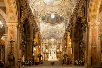 Interior de una catedral con nave central, columnas doradas y de mármol, bóvedas pintadas y un altar mayor ornamentado con arreglos florales