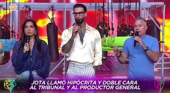 Jota Benz, una mujer y otro hombre, todos con micrófonos, en un set de televisión con luces rojas y amarillas; se ven sacos de boxeo colgando al fondo
