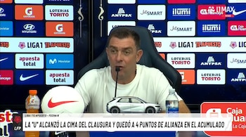 Un hombre con camiseta blanca habla frente a un micrófono en una conferencia de prensa con un panel de patrocinadores detrás