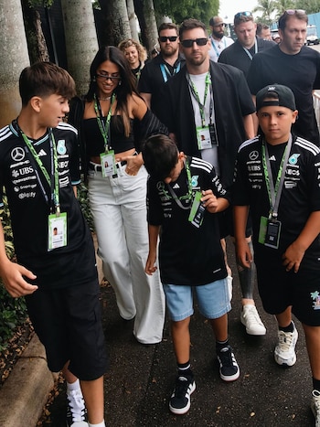 Lionel Messi, Antonela Roccuzzo y sus hijos caminan al aire libre, llevando pases VIP del Paddock Club de F1 y camisetas del equipo Mercedes