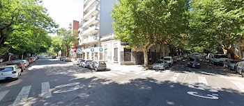 Calle urbana con edificios, automóviles estacionados junto al cordón y árboles sobre la vereda