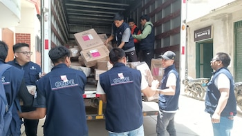 Trabajadores con chalecos azules del organismo electoral ONPE descargan cajas de cartón con etiquetas del contenedor de un camión