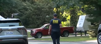 Persona con camiseta de "State Police Fire Investigator", SUV Chevrolet gris, camioneta Ford roja, remolque blanco, árboles y calle