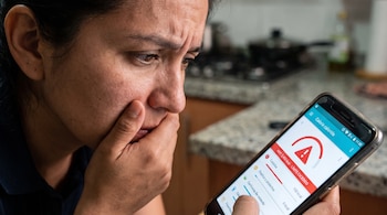 Primer plano de una mujer mirando un teléfono móvil con una aplicación de seguimiento de calorías que muestra un aviso de límite excedido.