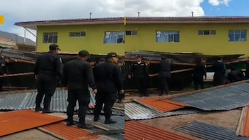 Varios uniformados de negro levantan láminas onduladas de metal caídas en el suelo frente a un edificio amarillo