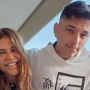 Una mujer de cabello largo rubio sonriendo junto a un joven con pelo corto oscuro, bigote tenue, arete y tatuaje en el cuello