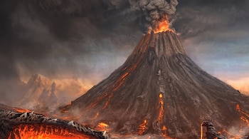 Un volcán en erupción lanza humo y ceniza al cielo gris mientras ríos de lava incandescente bajan por sus laderas rocosas.