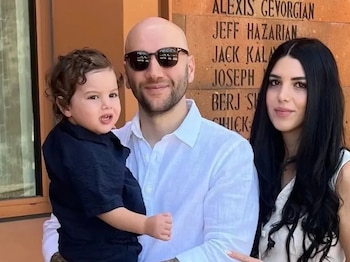 Un hombre calvo con gafas de sol sostiene a un niño pequeño de cabello rizado; una mujer con cabello oscuro y largo está a su derecha, posando para la cámara