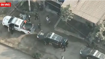 Vista aérea de un operativo policial con varias patrullas y agentes uniformados rodeando una casa en una calle residencial durante una transmisión en vivo