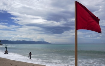 Un hombre camina en la playa cerca de una bandera roja como aviso del fuerte oleaje en el malecón de Puerto Vallarta (México). Imagen de archivo. EFE/ Arturo Montero
