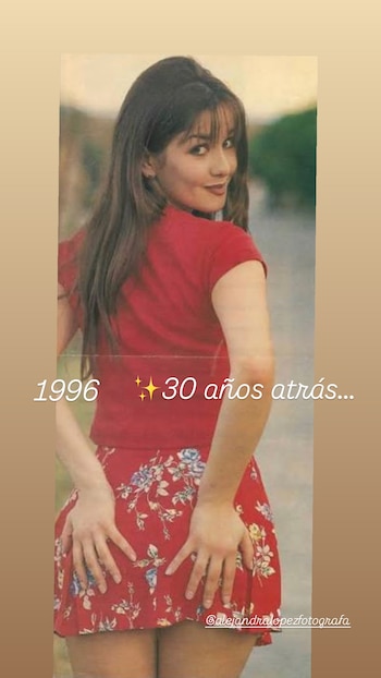 Una mujer joven con cabello castaño largo y flequillo, viste camiseta roja y minifalda floreada, posa de espaldas mirando hacia atrás con una sonrisa