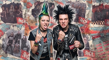 Una mujer con cresta verde y un hombre con cabello erizado y chaqueta de cuero posan entre recortes de fotos de grupos de rock.