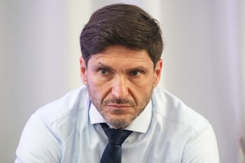 Primer plano de un hombre con barba corta, camisa clara y corbata oscura sobre un fondo de tonos claros