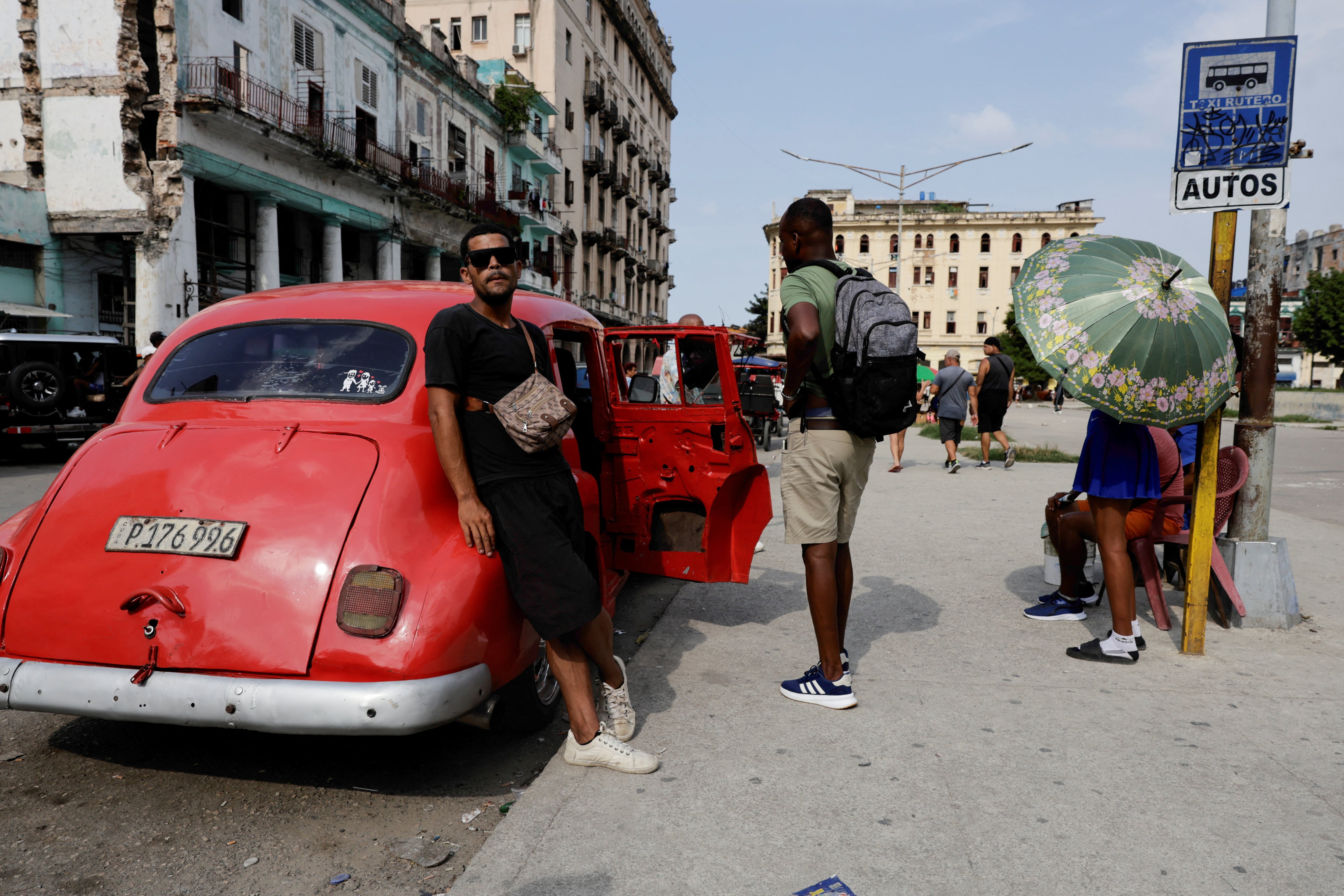 Un hombre se apoya en un automóvil clásico utilizado como taxi mientras el conductor espera más pasajeros, en un momento en que Cuba abre cautelosamente su sector energético a la inversión privada —tras la imposición por parte de Estados Unidos de un bloqueo petrolero contra el gobierno de la isla, aunque autorizando a empresas estadounidenses a exportar combustible a negocios privados—, en La Habana, Cuba, el 21 de julio de 2026. REUTERS/Norlys Perez