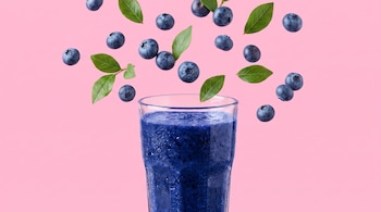 Un vaso de jugo de arándanos en primer plano. Arándanos y hojas verdes flotan sobre un fondo rosa liso.