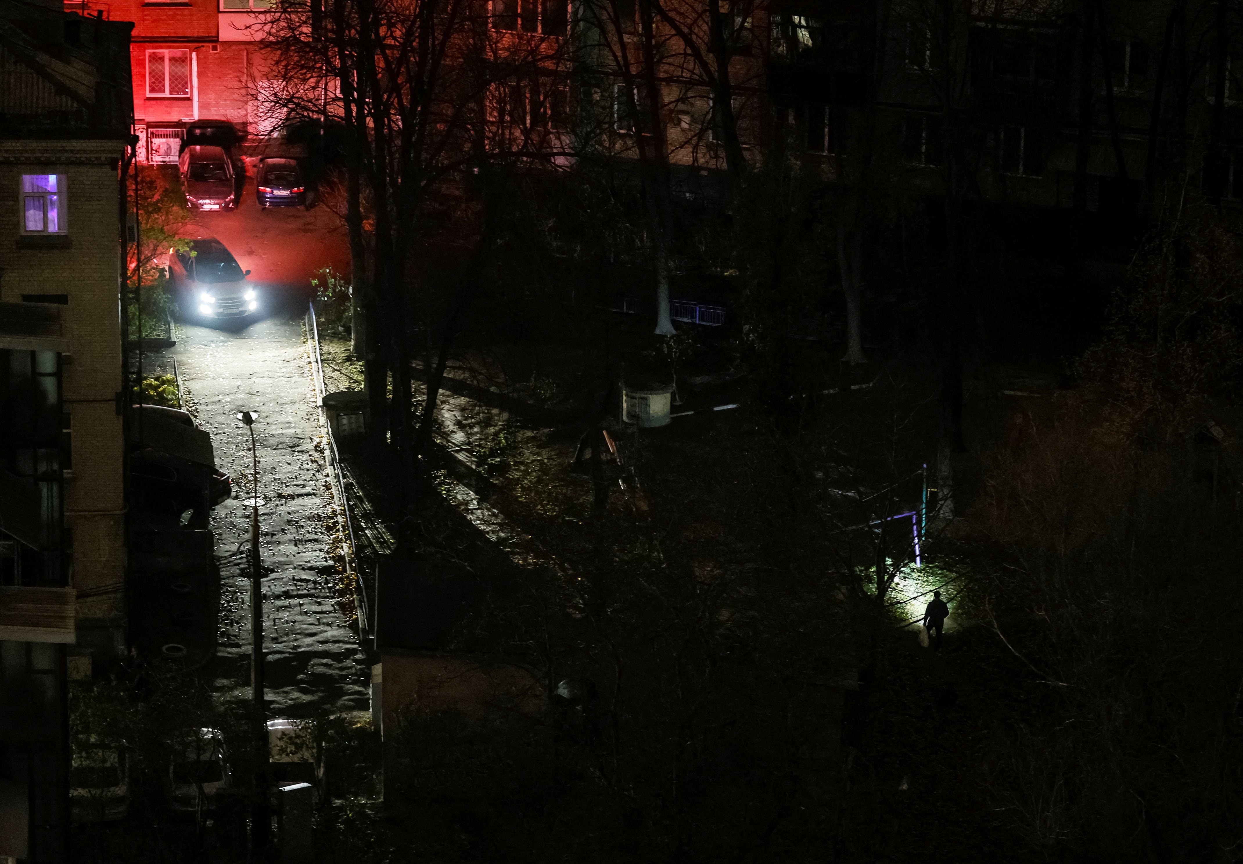 Un coche pasa junto a un vecino que camina con una linterna junto a unos edificios residenciales durante un corte de electricidad, en medio del ataque de Rusia a Ucrania, en Kiev (Ucrania) (REUTERS)