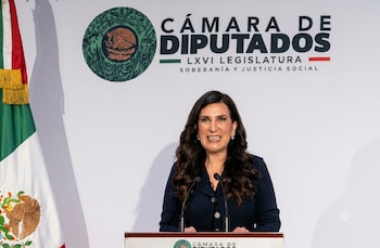Kenia López Rabadán sonríe en un podio con dos micrófonos. Detrás, logo y nombre de la Cámara de Diputados de México y la bandera nacional