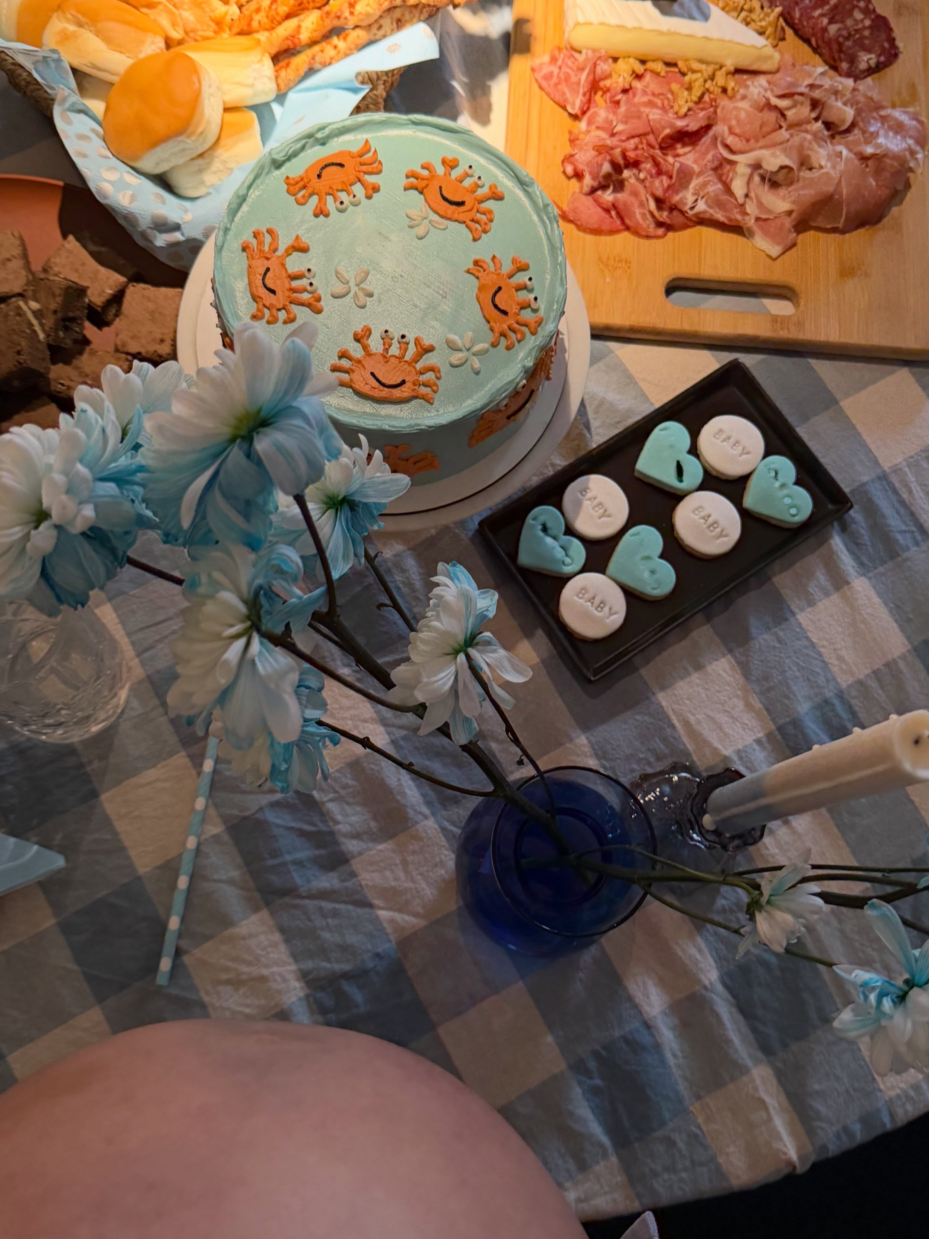 La mesa de un baby shower íntimo de Sofía Aldrey exhibe una torta decorada, galletitas temáticas, una variedad de alimentos y flores