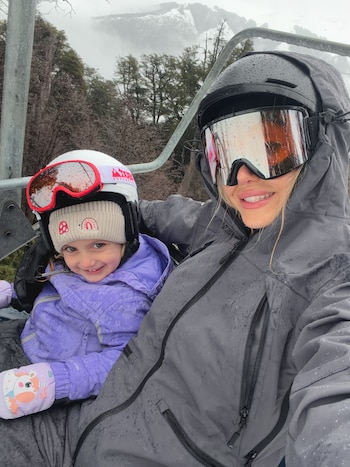 Cande Ruggeri y su hija, equipadas con ropa de abrigo, cascos y antiparras, posan sonrientes en la telesilla de un centro de esquí