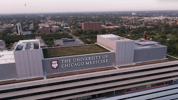 Vista aérea de un edificio con el letrero de la Universidad de Chicago Medicina, un emblema rojo y un helicóptero estacionado en la azotea