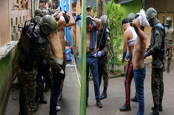 Varios hombres con las manos en la cabeza son inspeccionados por personal militar equipado con cascos y uniformes de camuflaje.