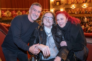 Julio Bocca, Charly García con gafas y bigote, y una mujer pelirroja posan sonrientes en el interior de un teatro con asientos rojos y público de fondo