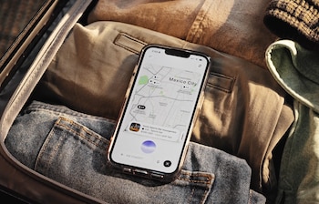 Teléfono móvil con aplicación de ChatGPT en pantalla, mostrando un mapa de la Ciudad de México con negocios destacados. El teléfono está sobre ropa en una maleta abierta
