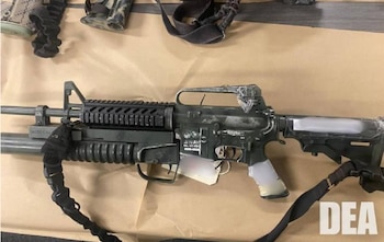 Un rifle semiautomático oscuro con lanzagranadas, correa negra y cinta adhesiva, sobre una superficie marrón. El logotipo de la DEA aparece en la esquina inferior derecha