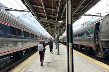 Vista de un andén de tren con dos trenes Amtrak plateados a los lados, y personas caminando bajo un techo de estación de madera