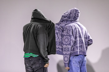 Dos personas de espaldas con capuchas. Sudaderas, una gris y otra morada con patrón, unidas por cremallera central. Llevan vaqueros