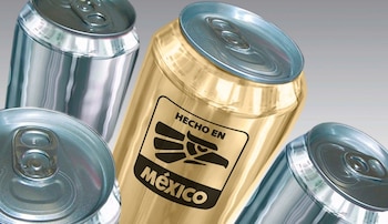Primer plano de una lata dorada con el logotipo "Hecho en México" en negro, rodeada de tres latas de aluminio plateadas en un fondo gris