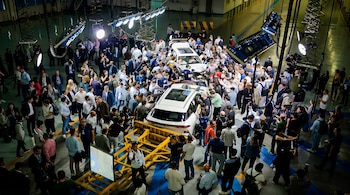 Vista aérea de una sala grande con dos SUVs Chery Tiggo 9 blancos rodeados por cientos de personas, con equipo de iluminación profesional sobre ellos