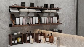 Vista detallada de un baño con estantes de madera oscura llenos de productos de cuidado personal, cepillos, velas y pequeños altavoces sobre un mostrador de mármol.