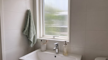 Lavabo blanco con grifo, dispensador de jabón, vaso con cepillos de dientes, toalla verde colgada y ventana con vidrio acanalado.