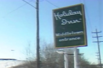 Cartel verde con texto blanco que dice 'Holiday Inn Middletown entrance'. Se observa un cielo azul, postes de servicios y vegetación invernal al fondo