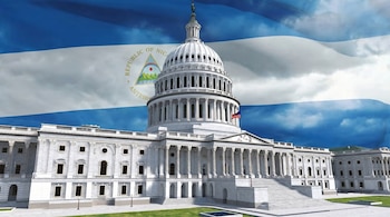 El Capitolio de EE. UU., un edificio blanco con cúpula y columnas, se ve desde una perspectiva frontal con una gran bandera de Nicaragua superpuesta en el cielo.