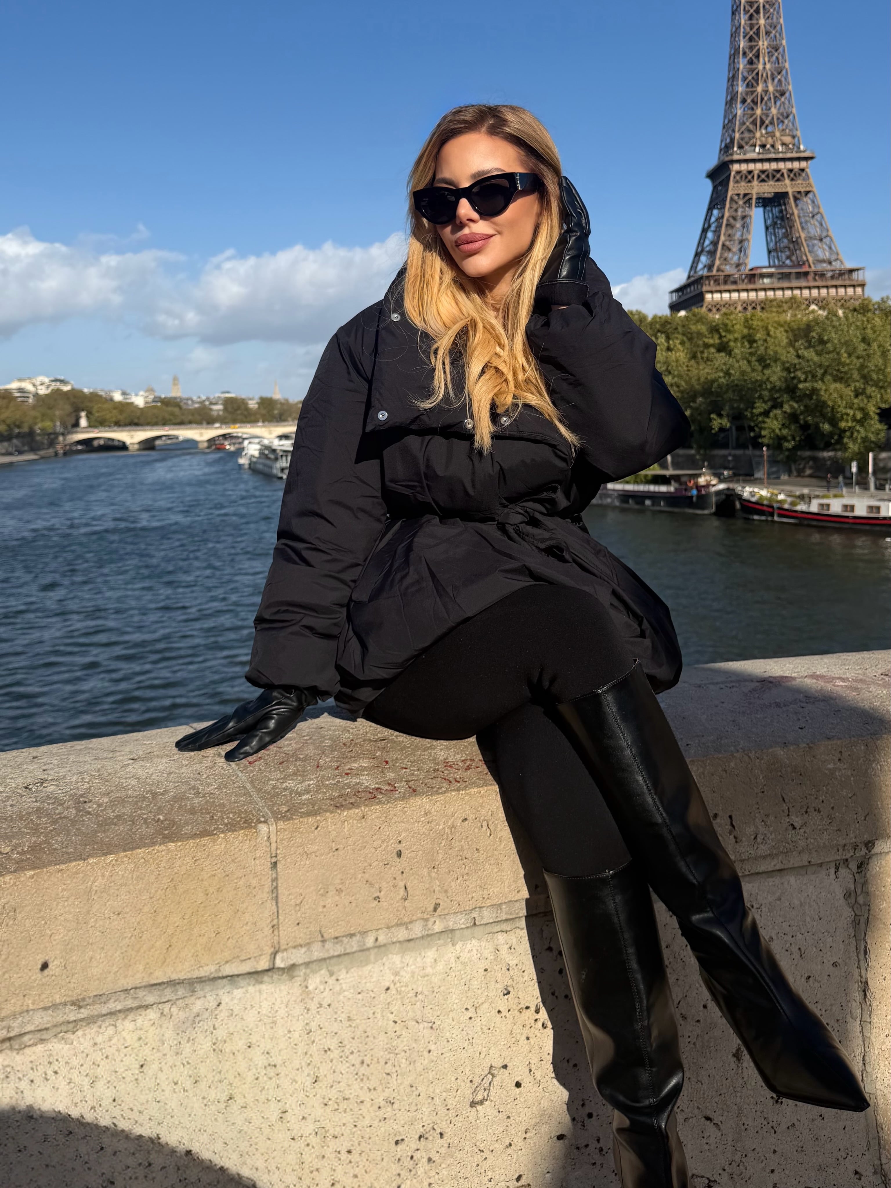 Anderson posa sentada sobre un pretil junto al río Sena con la Torre Eiffel