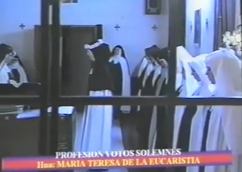 Varias religiosas con hábitos blancos y negros permanecen en fila dentro de una sala tras un ventanal con texto superpuesto