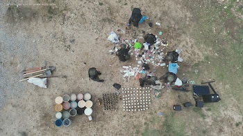 Seis individuos uniformados en terreno de tierra. Tres palas, un pico, cajas, bolsas, objetos dispersos. Dieciséis cubetas, decenas de botellas, una computadora y altavoces