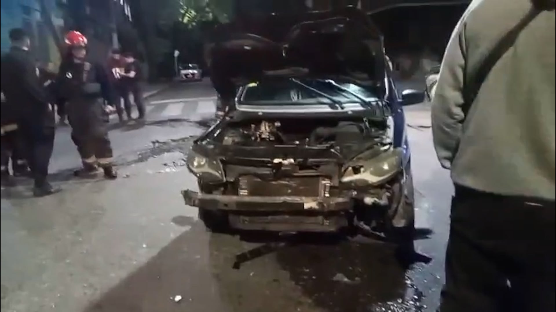 Un vehículo gravemente dañado con el capó abierto y escombros en la calle es atendido por personal de emergencia tras un choque y vuelco en Barracas.