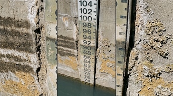 Regla graduada con números colocada en una pared de concreto erosionado junto a una superficie de agua.
