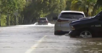 Una calle inundada por la que circulan vehículos con el agua hasta la mitad de las ruedas